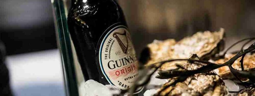 Bottiglia di birra Guinness Draught accanto a ingredienti per ricette salate tradizionali irlandesi.